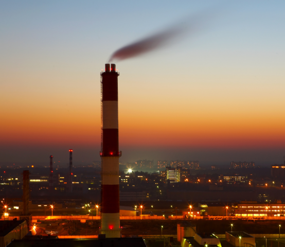 Industrial facility smokestack during sunset representing emissions monitoring and environmental compliance operations.