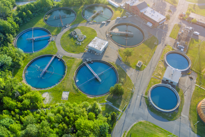 Aerial view of a modern industrial water treatment facility with multiple circular treatment tanks surrounded by greenery and access roads.